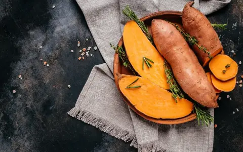 Pomarańczowe bataty, pokrojone i w całości, ozdobione ziołami. Ich bogate bataty wartości odżywcze czynią je idealnym składnikiem zdrowej diety.