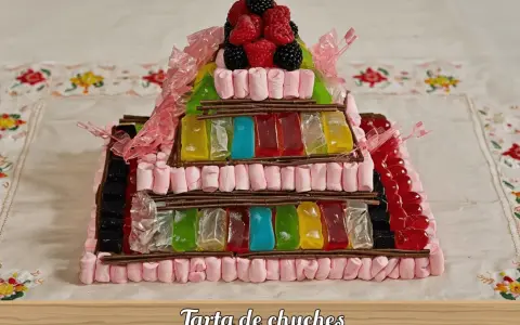 Una pirámide de tartas de gominolas, con capas de malvaviscos rosas, gominolas de colores y frutos rojos en la cima.