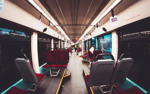 Wnętrze wagonu kolejowego z czerwonymi siedzeniami i uchwytami.