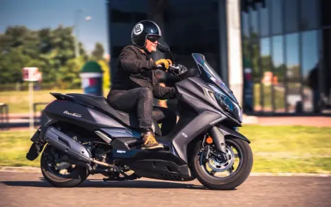 Mężczyzna w kasku jedzie na skuterze Kymco Downtown 125. Poznaj kymco downtown 125 dane techniczne.