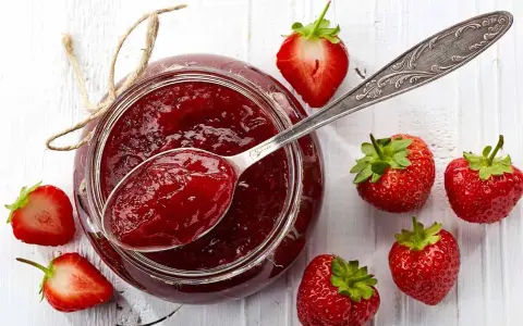 Glas mit Erdbeermarmelade, gesüßt mit Xylit, daneben frische Erdbeeren und ein Löffel Marmelade.