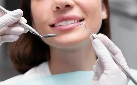 Uśmiechnięta kobieta podczas zabiegu remineralizacji szkliwa. Dentysta używa lusterka i sondy.