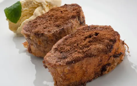 Dos torrijas de chocolate espolvoreadas con cacao y azúcar, acompañadas de helado de vainilla y una hoja de menta.