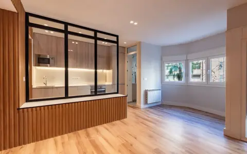 Entrada salón recibidor integrado. Cocina moderna con cristalera y madera, conectada a un luminoso salón con ventanas.