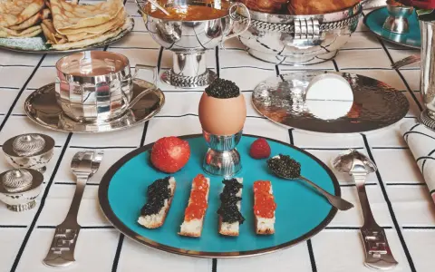 Un service de table à la française élégant pour un petit-déjeuner luxueux : toasts au caviar, œufs, fruits et crêpes.