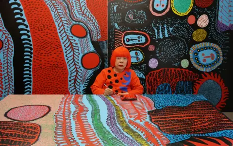 Yayoi Kusama jeune, entourée de ses œuvres psychédéliques vibrantes, peignant avec une concentration intense.