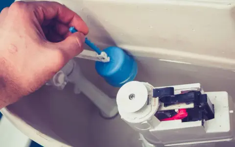 Main d'homme ajustant le flotteur bleu d'une chasse d'eau qui ne se remplit pas pour un wc suspendu.