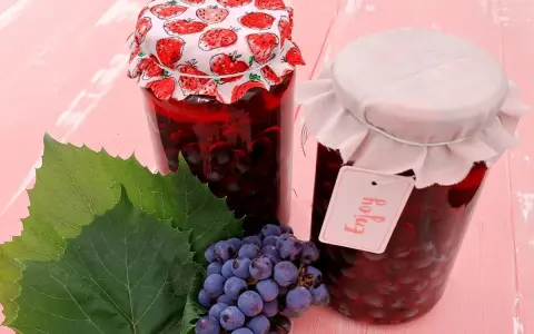 Słoiki z przetworami z winogron, przypominającymi wino z mrożonych winogron. Obok kiść winogron i liście.