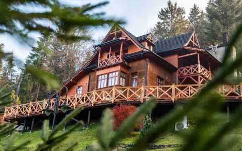 Drewniane schronisko turystyczne z tarasem i balustradą, otoczone drzewami.