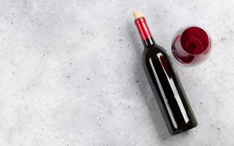 En flaska tamaral vin och ett glas rött vin på ett grått, stenig bakgrund.
