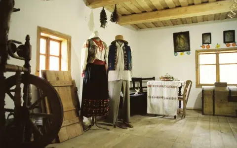 Tradycyjne stroje ludowe, kołowrotek i obrazy religijne tworzą klimat dawnej wsi. To żywa hel historia.