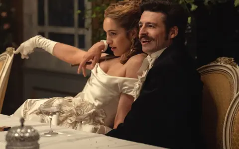 Elegancka para przy stole, zapowiedź nowych produkcji Netflix. Kobieta w białej sukni z rękawiczkami, mężczyzna w czarnym fraku.