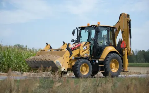 Żółta koparko-ładowarka CAT 432 w trakcie budowy drogi, z pełną łyżką ziemi.