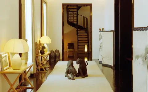Due sculture di pantere su un tappeto chiaro, in un corridoio elegante che ricorda la casa Giorgio Armani, con una scala a chiocciola sullo sfondo.