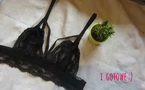 Czarny, koronkowy biustonosz typu bralette, idealny do obszywania bielizny. Obok mała roślinka w doniczce.
