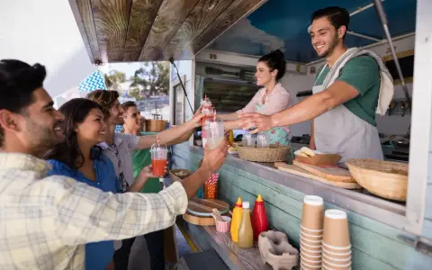 Uśmiechnięci ludzie odbierają napoje od barmanów z food trucka.