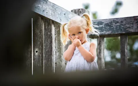 Mała dziewczynka z blond kucykami ssie kciuk, co może być sygnałem, że rodzice zastanawiają się, jak oduczyć dziecko ssania kciuka.