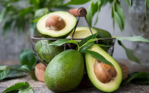 Des avocats frais, entiers et coupés en deux, dans un panier. Pour savoir comment avoir un avocatier qui donne des fruits, il faut de la patience et de bons soins.