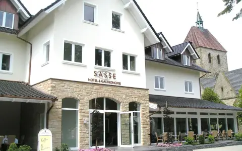 Gasthof Sasse in Soest mit Hotel & Gastronomie-Schild, Steinfassade und Kirche im Hintergrund.