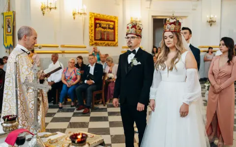 Uroczystość zaślubin w cerkwi. Pan młody, niczym ludowy grajek z Ukrainy, w eleganckim czarnym garniturze, z narzeczoną w białej sukni, przyjmują błogosławieństwo.