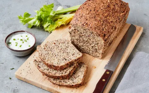 Ein rustikales Chia Brot, frisch aufgeschnitten, mit Sellerie und Dip auf einem Holzbrett.