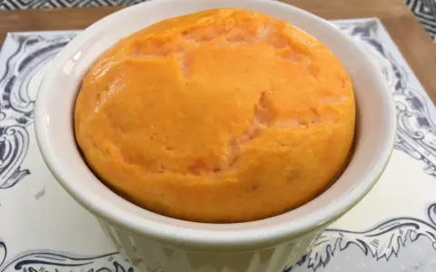 Un délicieux flan de carottes, doré et moelleux, servi dans un ramequin blanc sur une assiette décorée.
