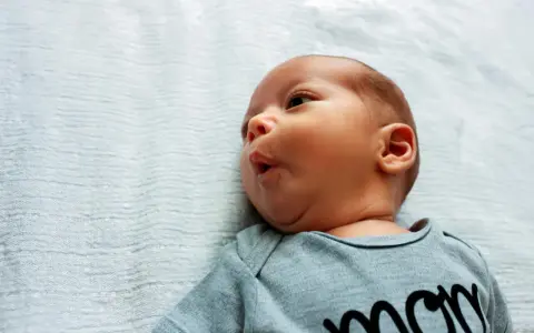 Noworodek z lekkim kręczem szyi i asymetrią twarzy, w szarym body z napisem "mom".