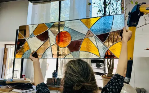 Un artiste admire son œuvre, un vitrail aux couleurs chaudes et géométriques, fruit d'un cours de vitrail.