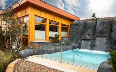 Entspannendes Wasserbecken mit Wasserfällen vor einer Holzhütte, ideal für eine H2O Sauna.