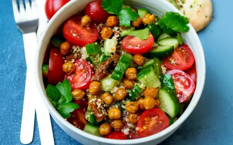 Frischer Couscous-Salat mit Kichererbsen, Tomaten und Gurken, garniert mit Petersilie.