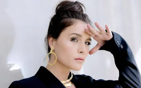 Jessie Ware, w czarnej marynarce, z dłonią na czole, jakby prosiła "say you love me". Złote kolczyki i naszyjnik dodają blasku.