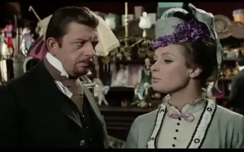 Mariusz Dmochowski w filmach, u boku pięknej kobiety w kapeluszu, w sklepie pełnym lalek i bibelotów.