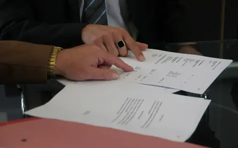Dwóch mężczyzn analizuje dokumenty. Jeden z nich, w garniturze i z pierścieniem na palcu, wskazuje na tabelę. Pytanie: Millennium Bank zajęcie egzekucyjne jak sprawdzić?