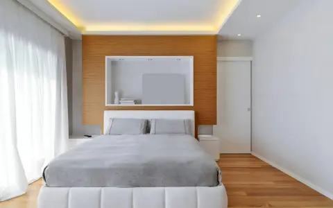 Camera da letto con letto bianco, lenzuola grigie e un moderno controsoffitto con illuminazione a LED.