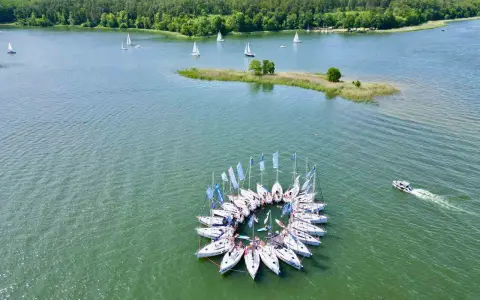 Żaglówki tworzą okrąg na jeziorze, otoczone lasem. To jedne z najpiękniejszych miejsc w Polsce – Mazury.