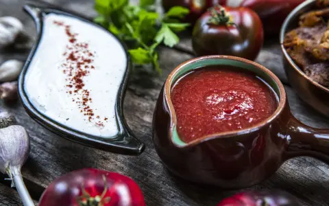 Två såser, en vit med paprika och en röd tomatbaserad, redo för ditt kebabsås recept. Tomater, vitlök och örter i bakgrunden.