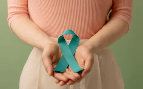 Dłonie trzymają turkusową wstążkę, symbolizującą wsparcie dla kobiet z PCOS. Dowiedz się, pcos co to.