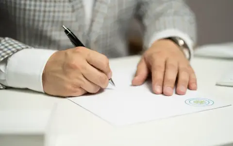Mężczyzna w garniturze pisze długopisem na dokumencie, który może być pozwem o podwyższenie alimentów.
