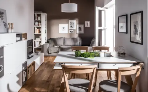 Nowoczesny salon z szarą kanapą i drewnianymi krzesłami. Czy brązowy pasuje do szarego? Tak, w tej aranżacji tworzy przytulną atmosferę.
