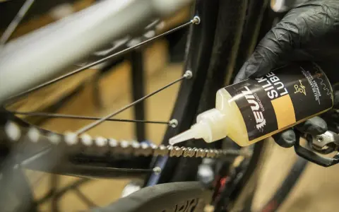 Rękawiczka z czarną rękawiczką aplikuje olej na łańcuch rowerowy, pokazując, jak nasmarować łańcuch w rowerze.