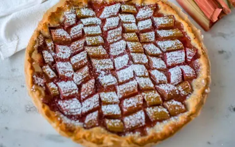 Tarta z rabarbarem posypana cukrem pudrem, obok łodygi rabarbaru.