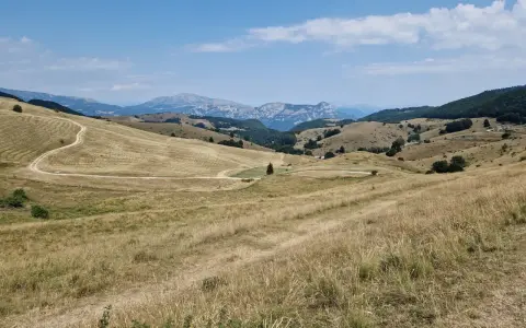Ampia vallata con erba secca e un sentiero tortuoso che sale verso il passo fittanze. Montagne sullo sfondo sotto un cielo azzurro con nuvole bianche.