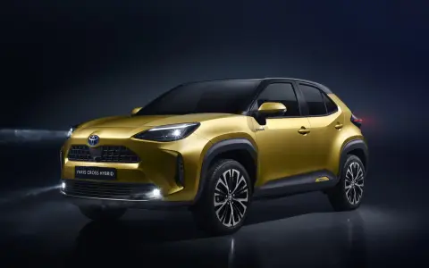 Złoty Toyota Yaris Cross Hybrid z włączonymi światłami na ciemnym tle.