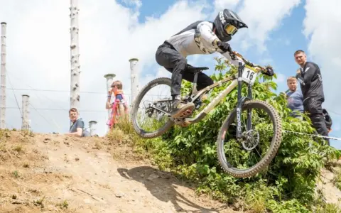 Downhill-Fahrer springt über eine Schanze bei den Dirt Masters Winterberg. Zuschauer beobachten das Spektakel.