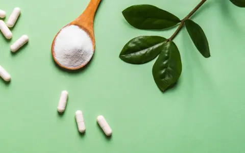 Vita C-vitaminer i kapslar och pulver på en sked, med gröna blad.