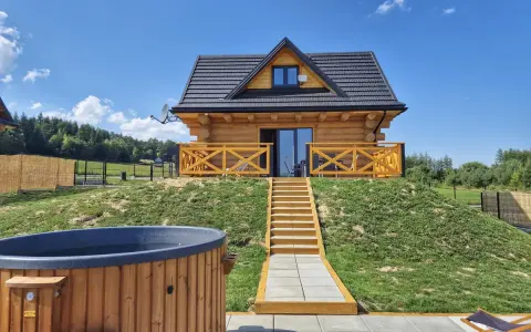 Uroczy domek na odludziu z drewnianą werandą i schodami prowadzącymi do drzwi. Przed domkiem jacuzzi i leżaki.