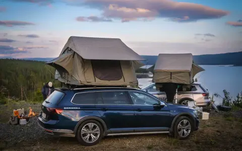 Två bilar med takboxar som fungerar som tält står redo för camping vid en sjö. En eld sprakar i förgrunden. En perfekt plats för camping i Gnesta.