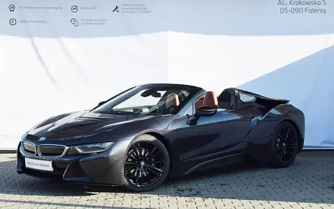 Ciemnoszary kabriolet BMW i8 z brązowym wnętrzem na tle białej ściany z logo BMW.