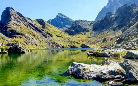 Lago alpino dalle acque smeraldine, incastonato tra montagne scoscese e verdi pendii. Un angolo di pace nell'Italia del Nord.