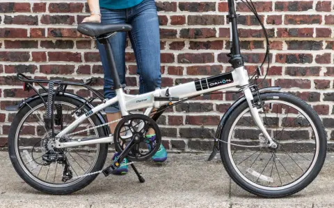 A person stands next to a silver Dahon Mariner folding commuting bike, ready for their next urban adventure.